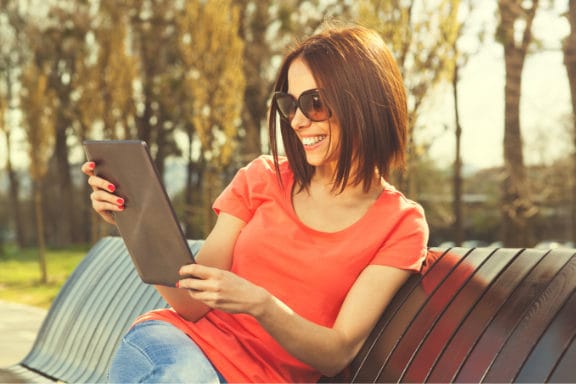 A woman sitting on a bench looking at a large tablet